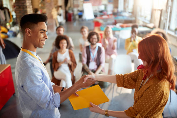young redhead female congratulates a student for successfully attending business seminar, giving him certificate in folder. selective focus image.